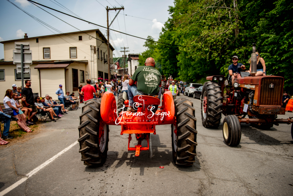 a tractor parade driver is seen from behind on his orange tractor driving down the main street in Callicoon NY