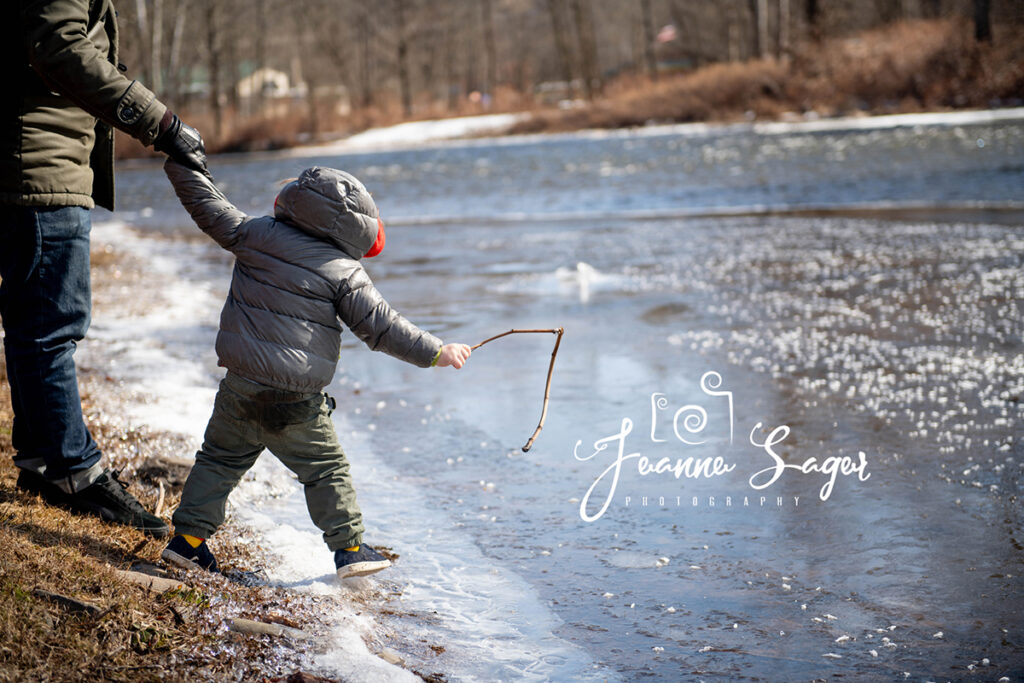 little boy holding his dad hands leans out with a stick over the frozen callicoon creek